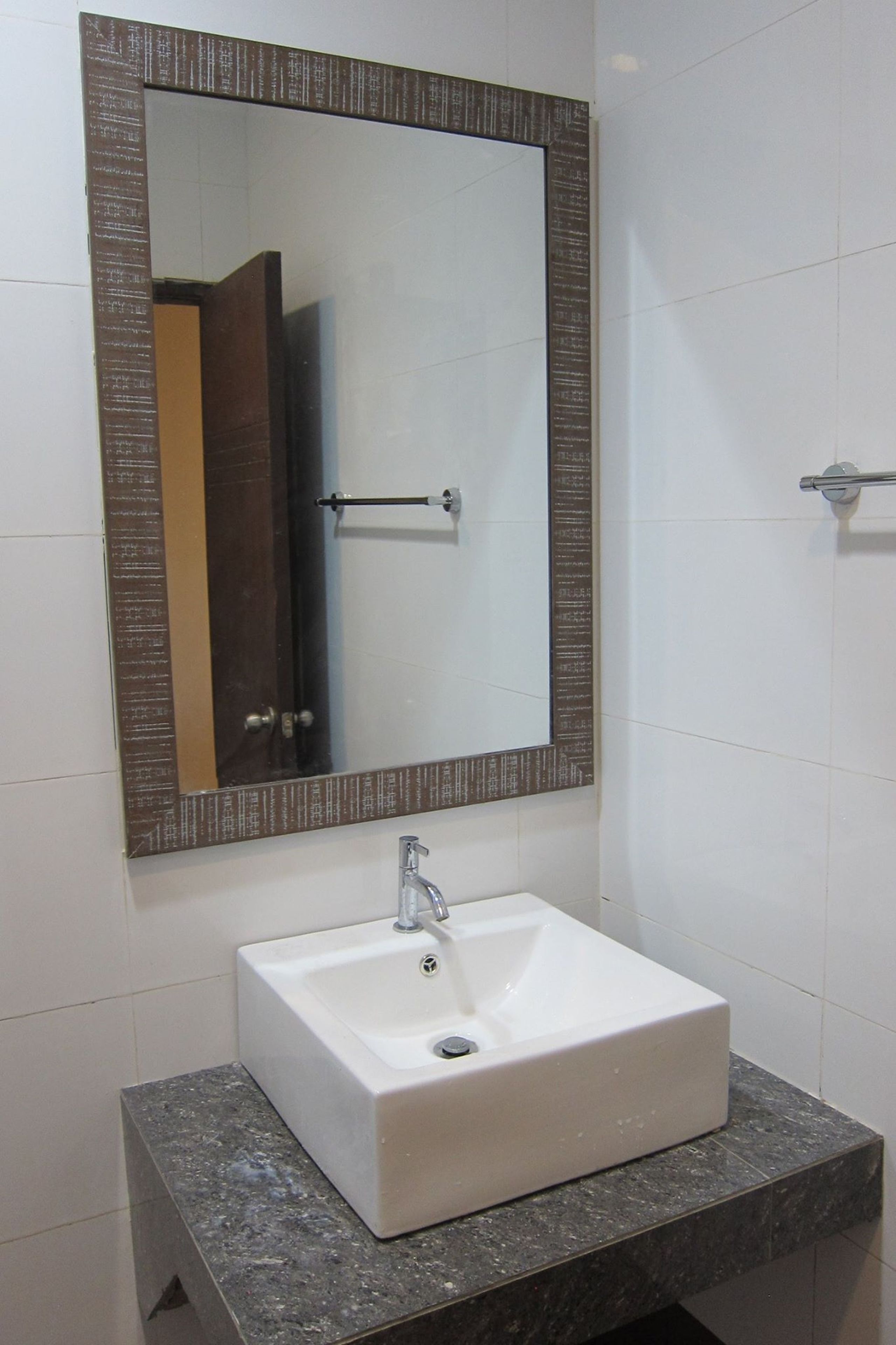 A bathroom with a white sink, a rectangular mirror with a decorative frame, and a towel rack.