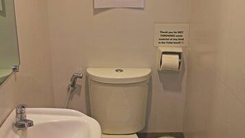 Un bagno piccolo con un water, un lavandino e una finestra. Segnaletica che indica di non gettare carta igienica o altri rifiuti nel water, ma di utilizzare il cestino.