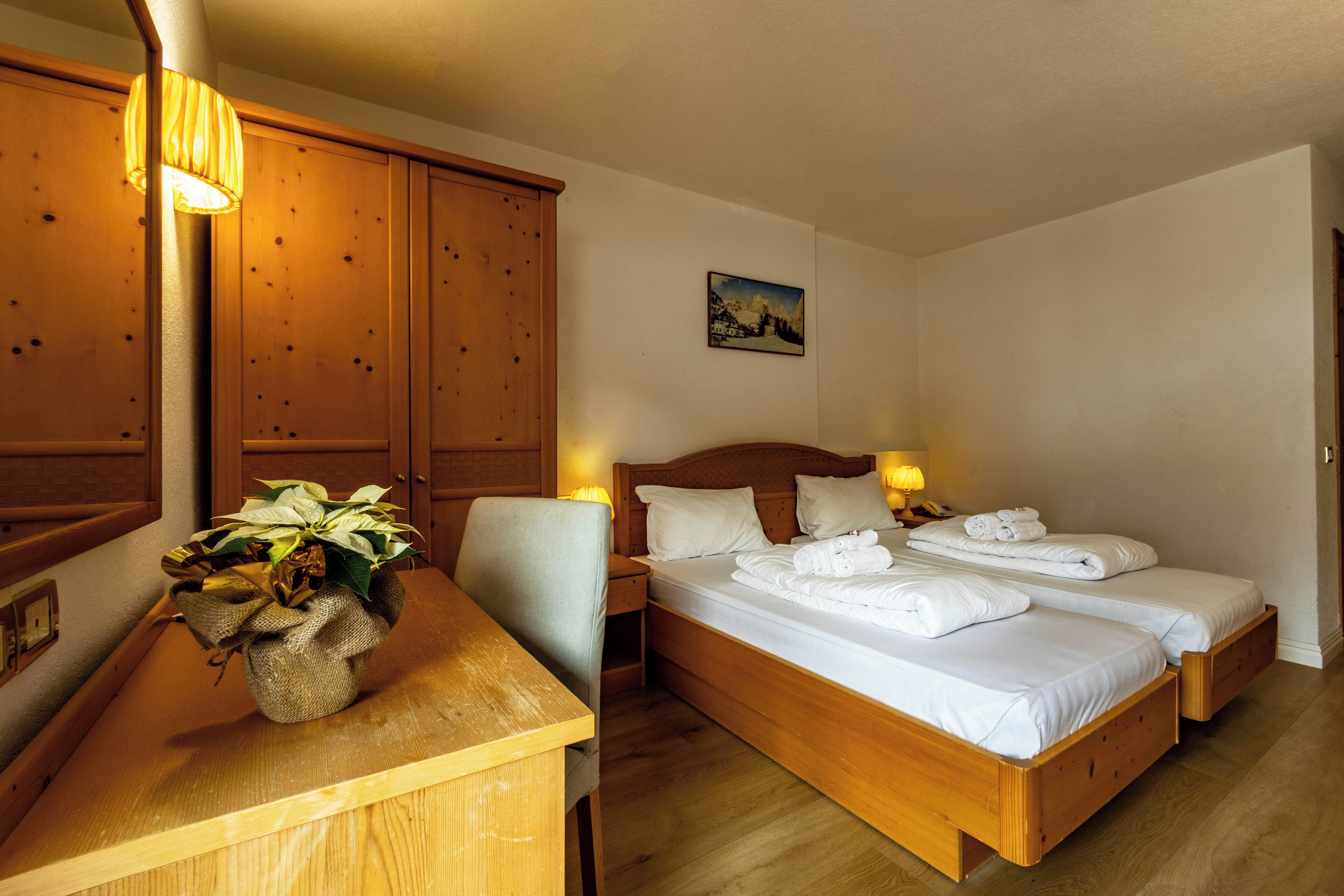 A hotel room with two wooden beds, a wooden desk, a lamp, and a wall-mounted picture.