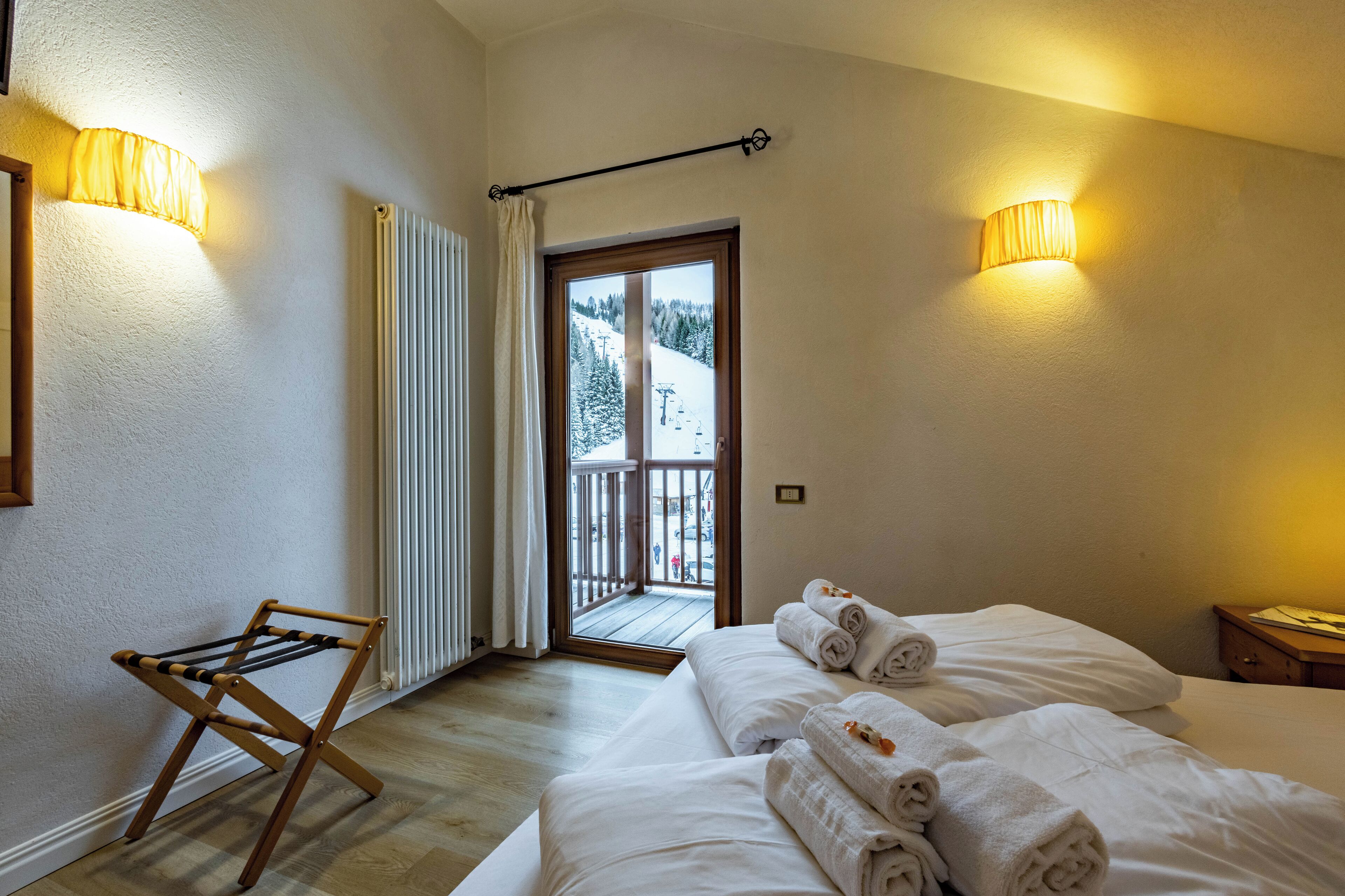 A hotel room with a bed, a drying rack, and two wall-mounted lamps.