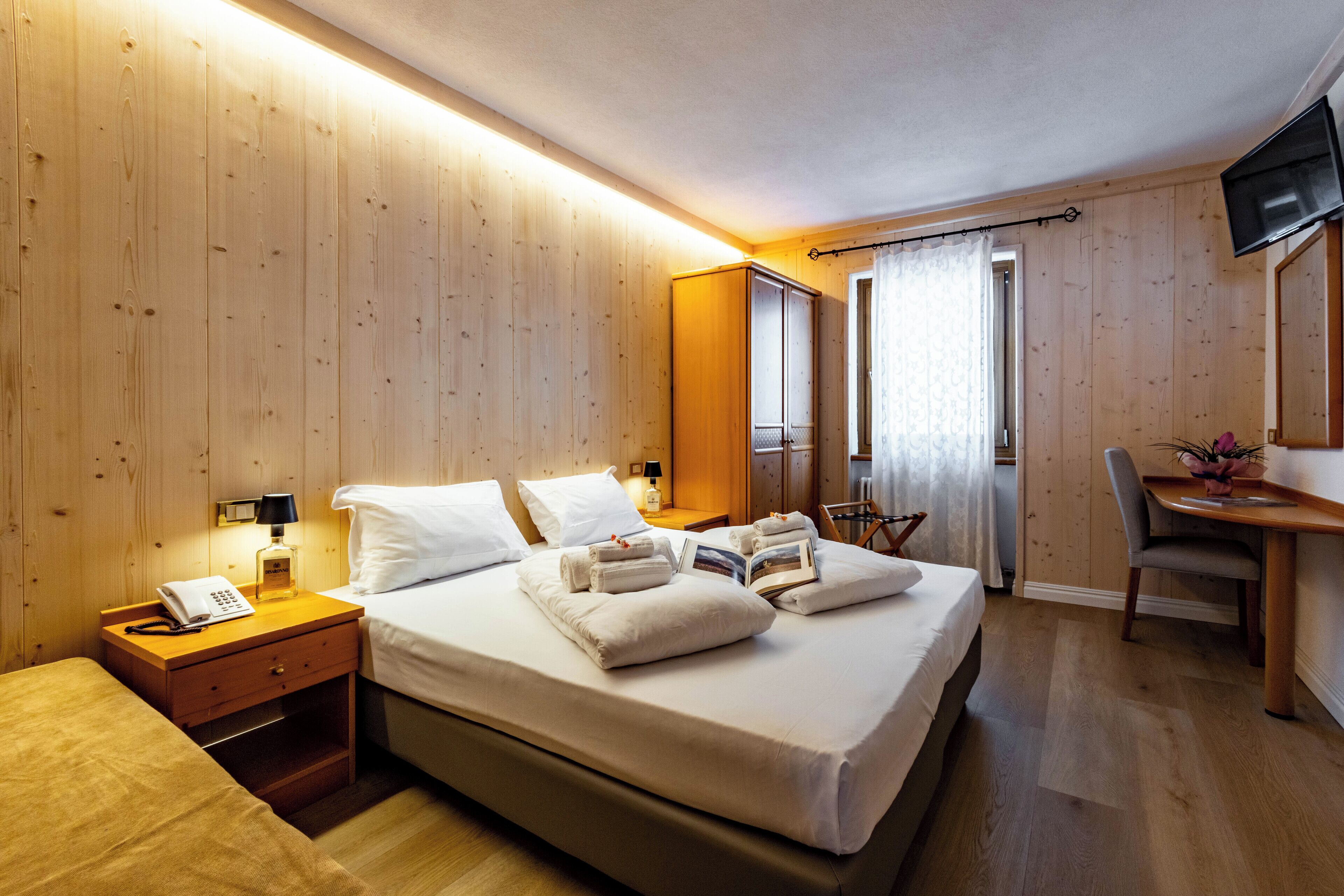 A hotel room with a wooden interior, a bed with white linens, a desk with a chair, and a television on the wall.
