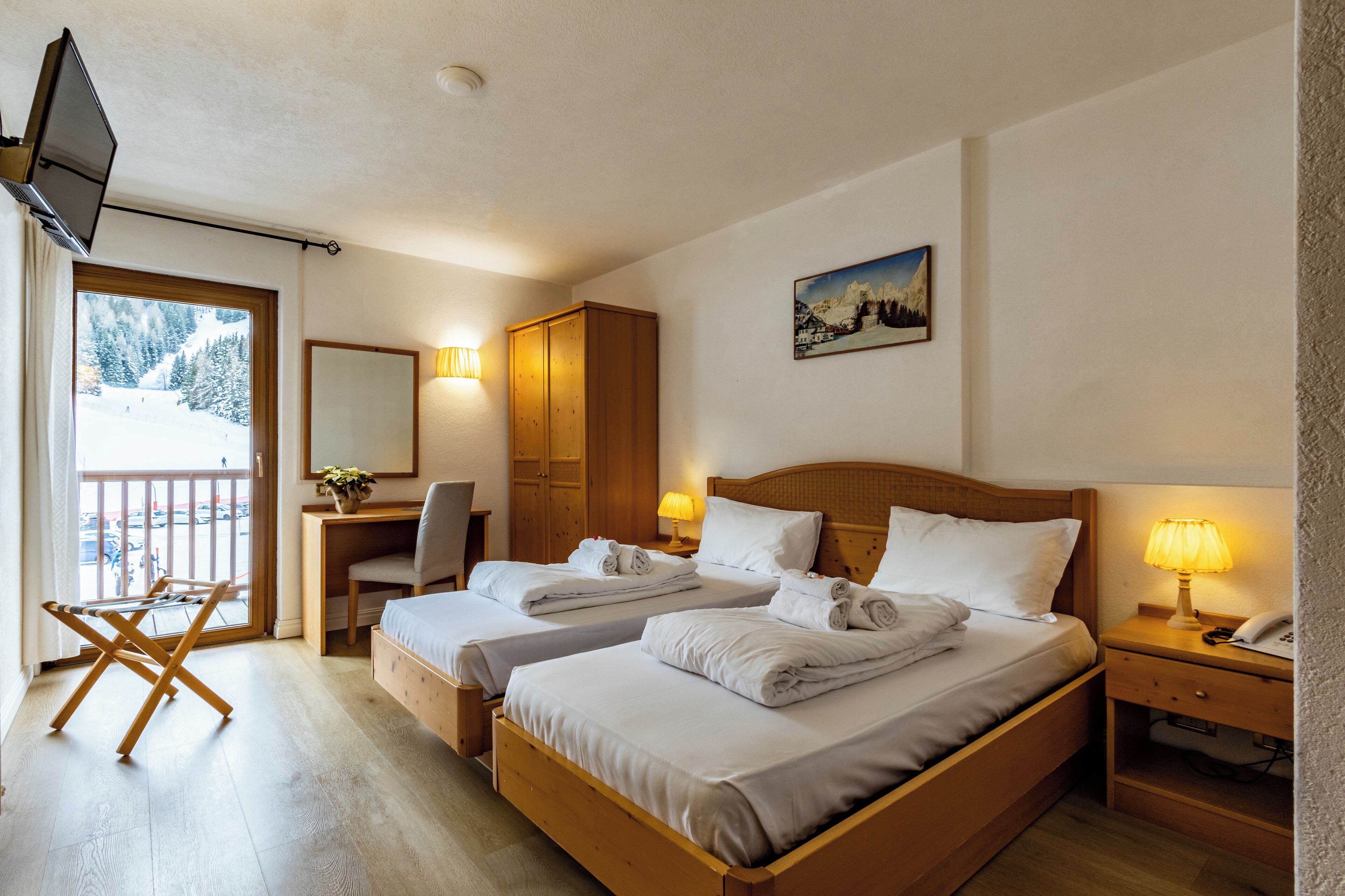 Une chambre d’hôtel avec deux lits, un bureau, une chaise, une télévision et un balcon donnant sur des arbres couverts de neige.