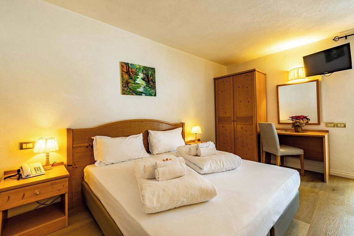 A hotel room with a large bed, a desk, a chair, a TV, and a painting on the wall.