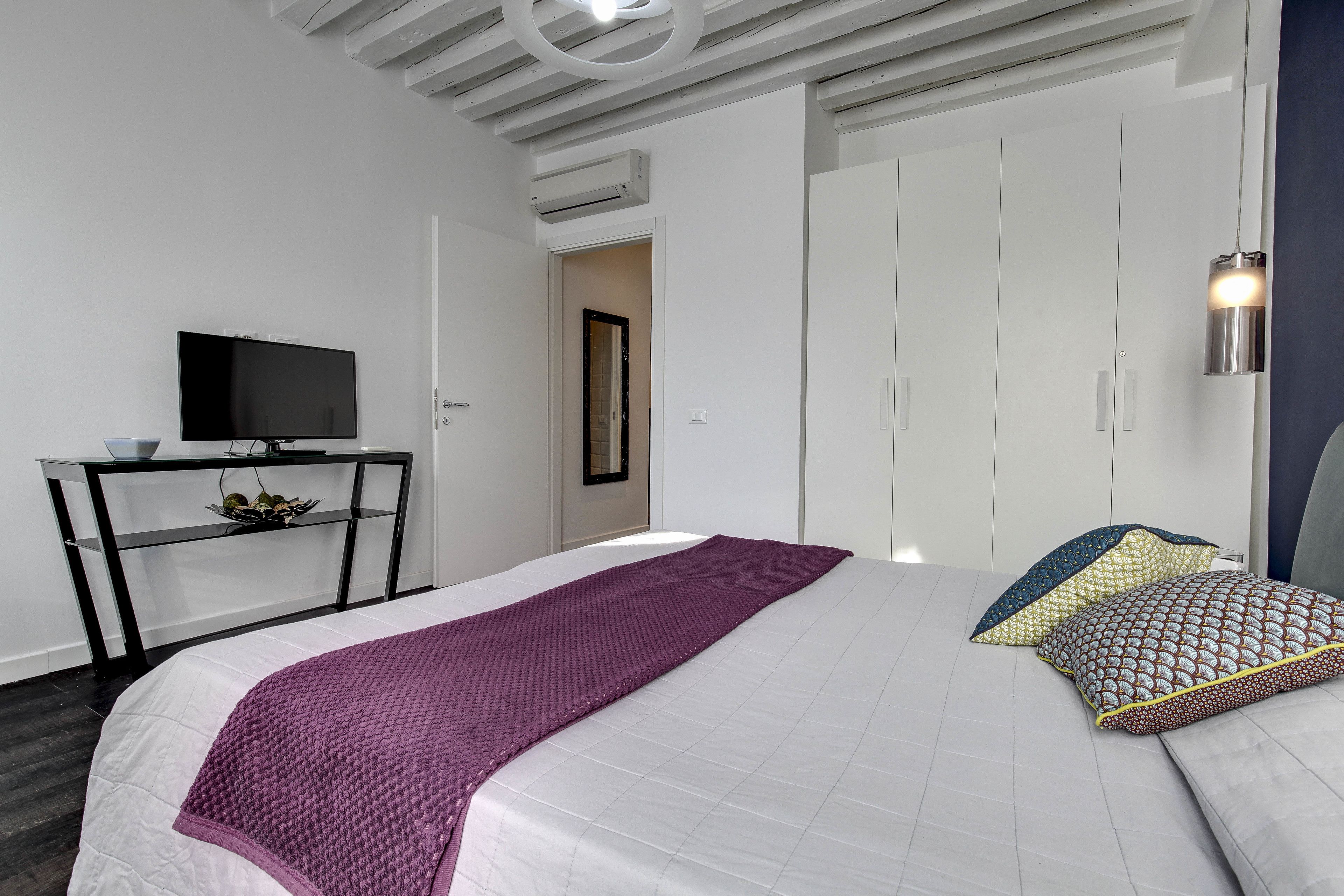 Une chambre à coucher moderne avec un lit, un téléviseur posé sur un meuble et une armoire.