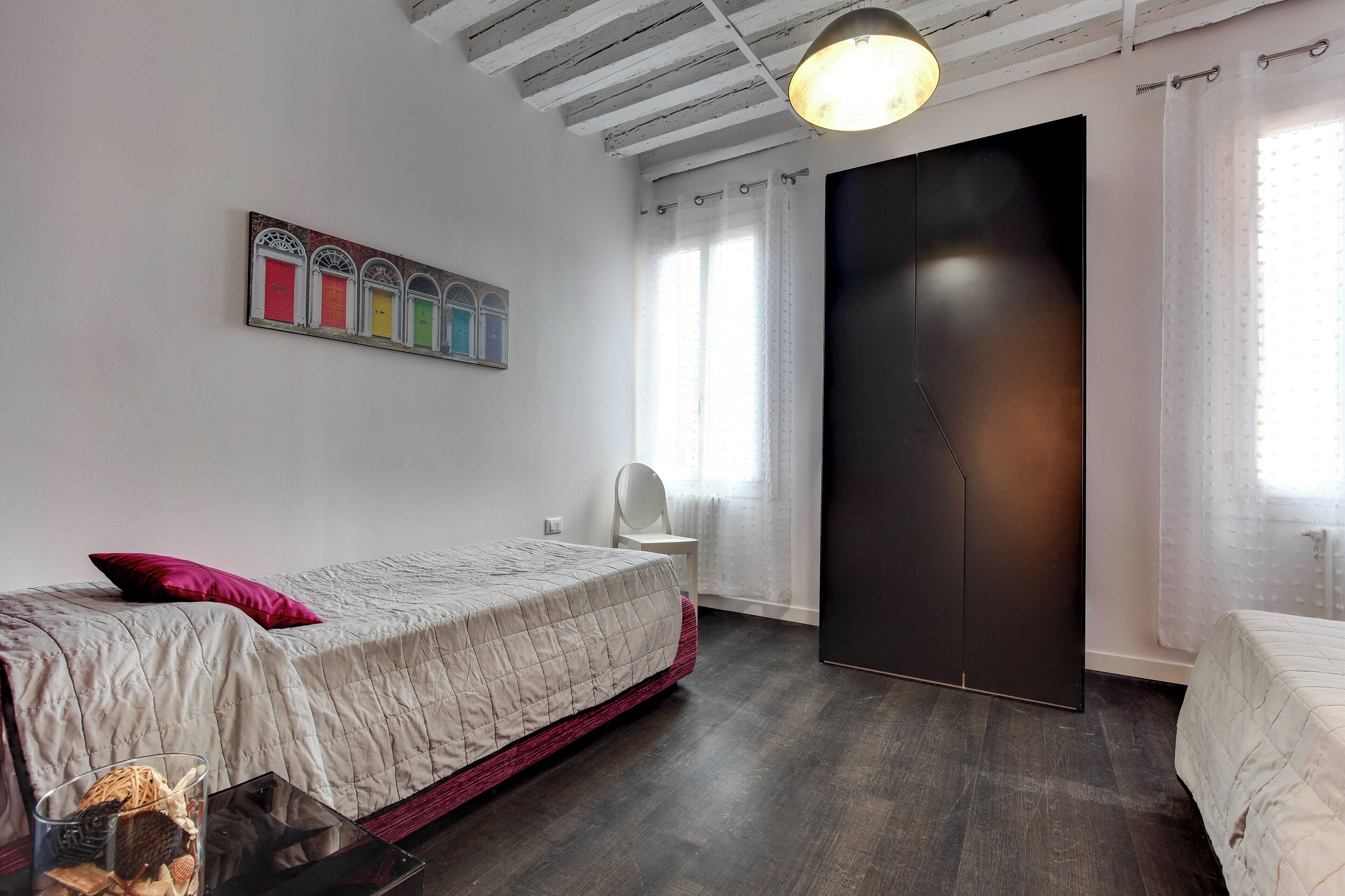 Een slaapkamer met een bed, een stoel, een kledingkast en een schilderij aan de muur.