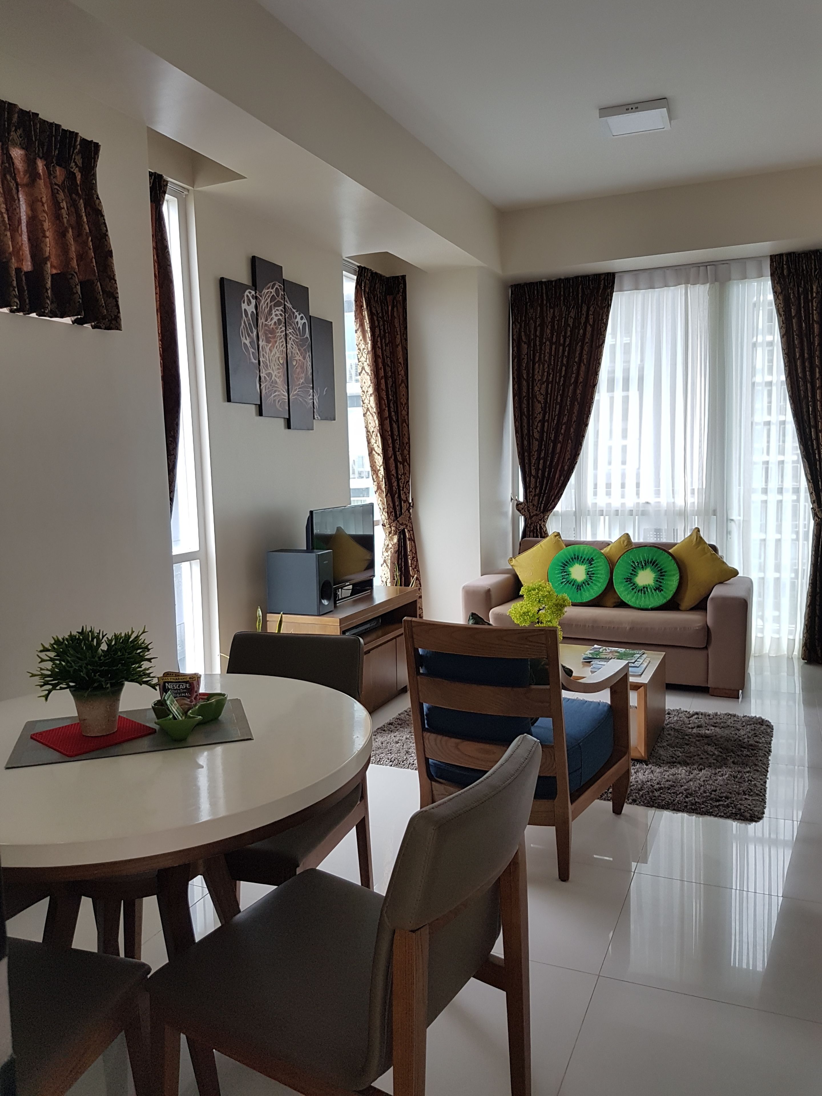 A modern living room with a dining area, featuring a sofa with green pillows, a flat-screen TV, and a coffee table.