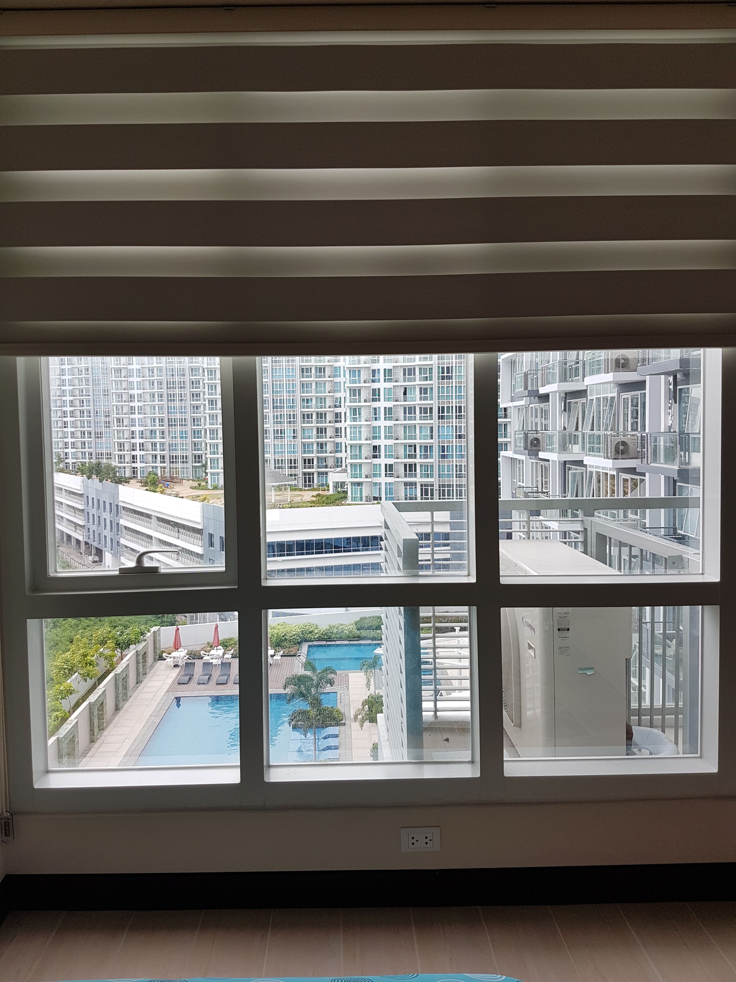 A room with a large window overlooking a modern building complex, a pool, and a water feature.