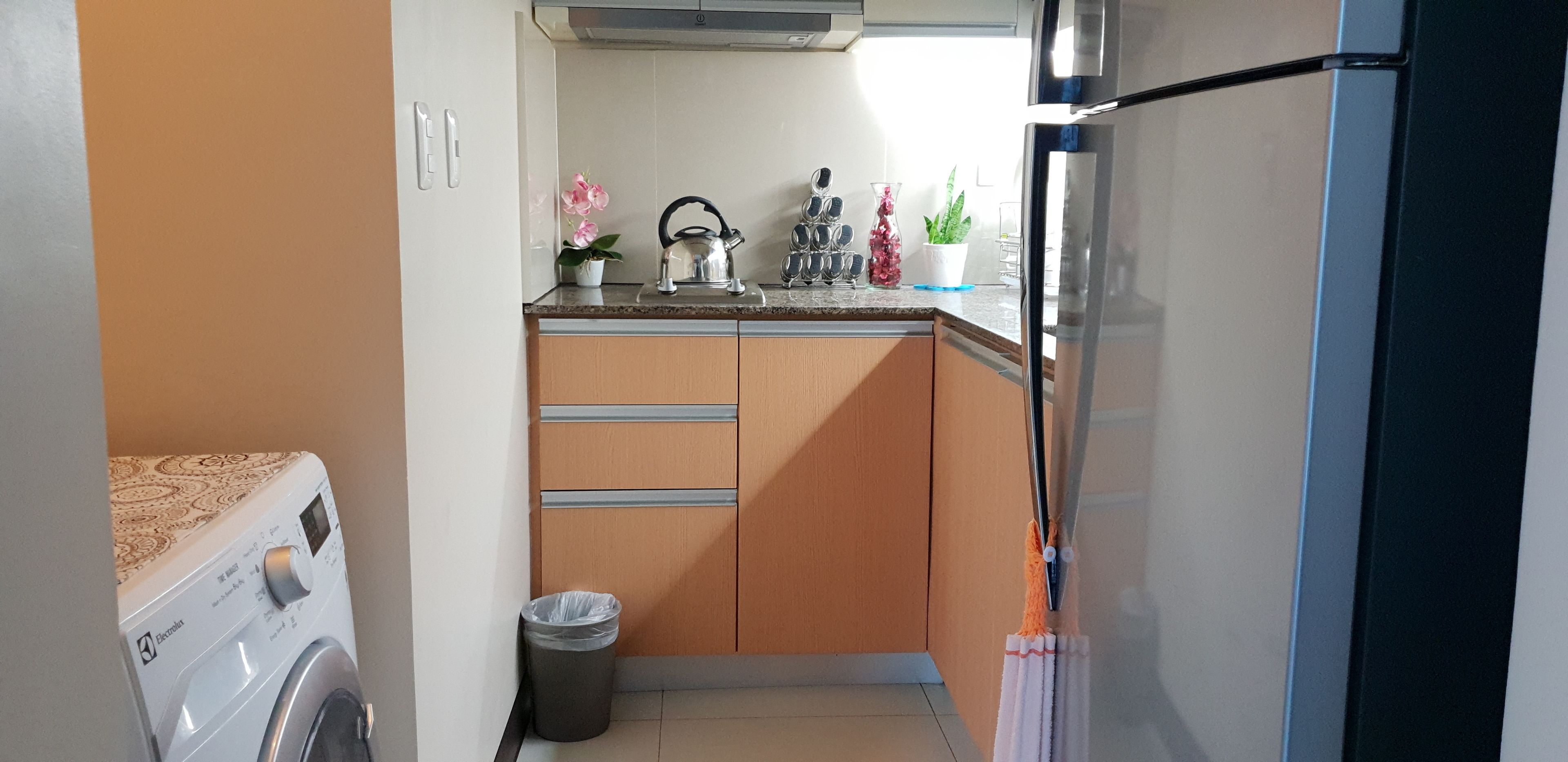A compact kitchen with a washing machine, a trash bin, and a refrigerator.