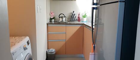 A compact kitchen with a washing machine, a trash bin, and a refrigerator.