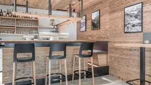 A bar area with wooden walls, black bar stools, and a wooden counter. - Hotel Mathiesn (Soelden)