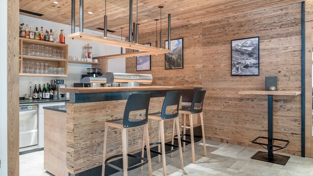 A modern bar area with wooden accents, bar stools, and a wine display. - Hotel Mathiesn (Soelden)