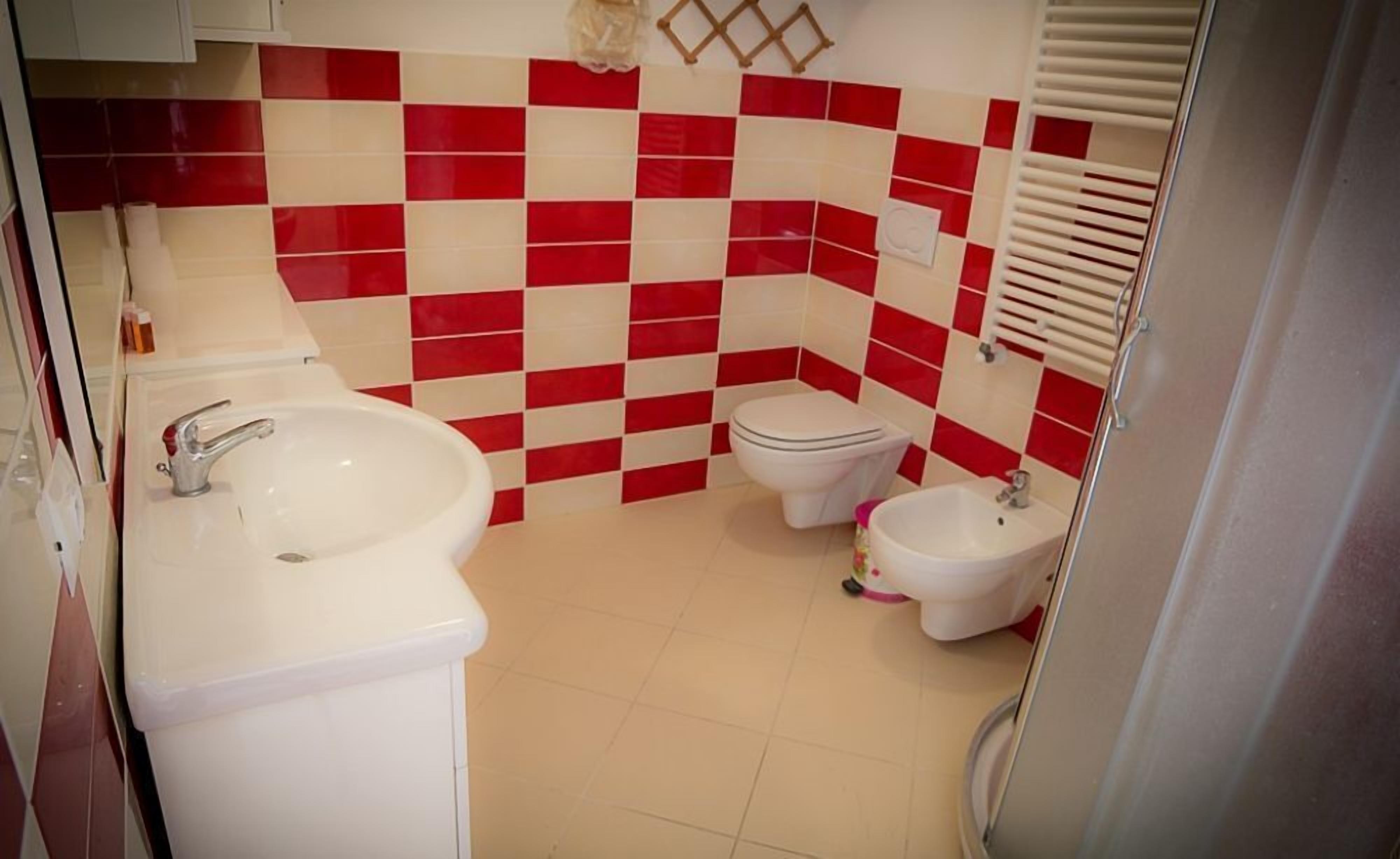 A bathroom with a checkered red and white tile wall, a white sink, a toilet, and a bidet.