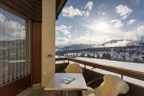 A balcony with a table and chair, overlooking a snowy mountain landscape. - T3 Alpenhotel Flims (Flims)