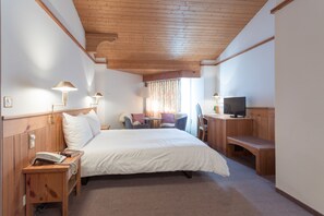 Ein Hotelzimmer mit Holzboden, einem Bett mit weißer Bettwäsche, einem Schreibtisch mit Fernseher und einem kleinen Tisch mit Stühlen.