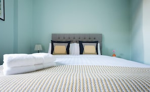 Een netjes opgemaakt bed met een gestreept dekbed, een gestoffeerd hoofdbord en twee kussens met geometrische patronen.