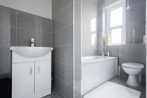 A modern bathroom with a white sink, a bathtub, and a toilet. - The Euston St Pancras Apartments (London)