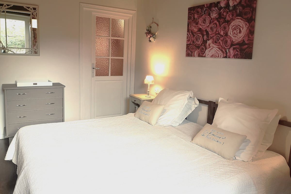 Une chambre à coucher comprenant un lit, une table de chevet, une lampe, une commode et une porte dotée de panneaux en verre dépoli.