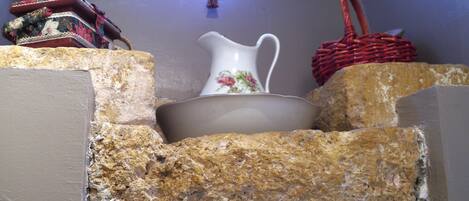 A stone wall with a white pitcher and a bowl on top, and a red woven basket to the right.