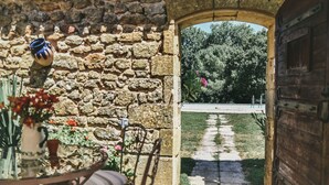An outdoor seating area with stone walls, a wooden door, and a pathway leading to a garden. - La Borie du Chevrier (Sainte Croix de Beaumont)