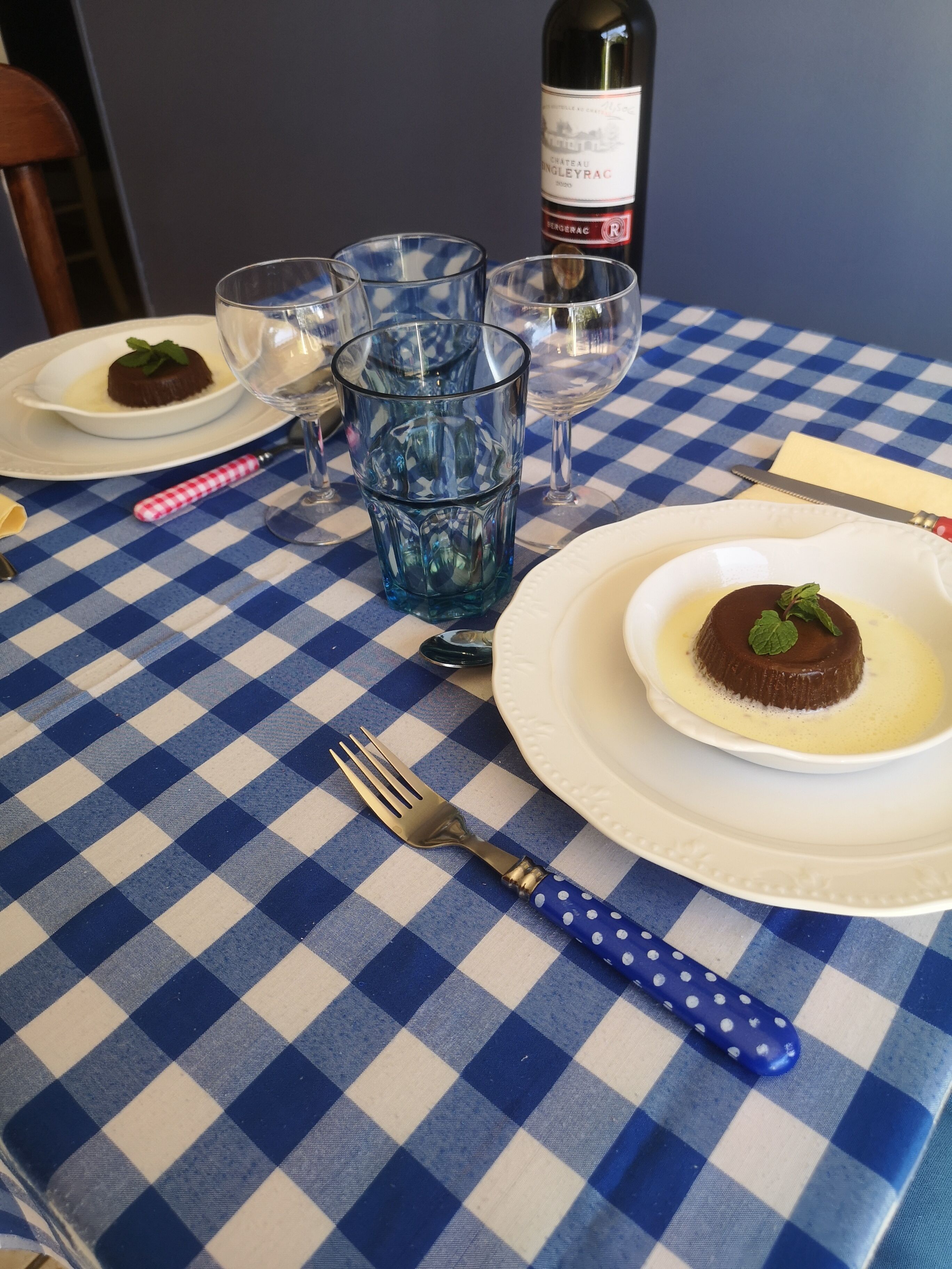 A table with a checkered tablecloth, a bottle of wine, and plates with desserts.