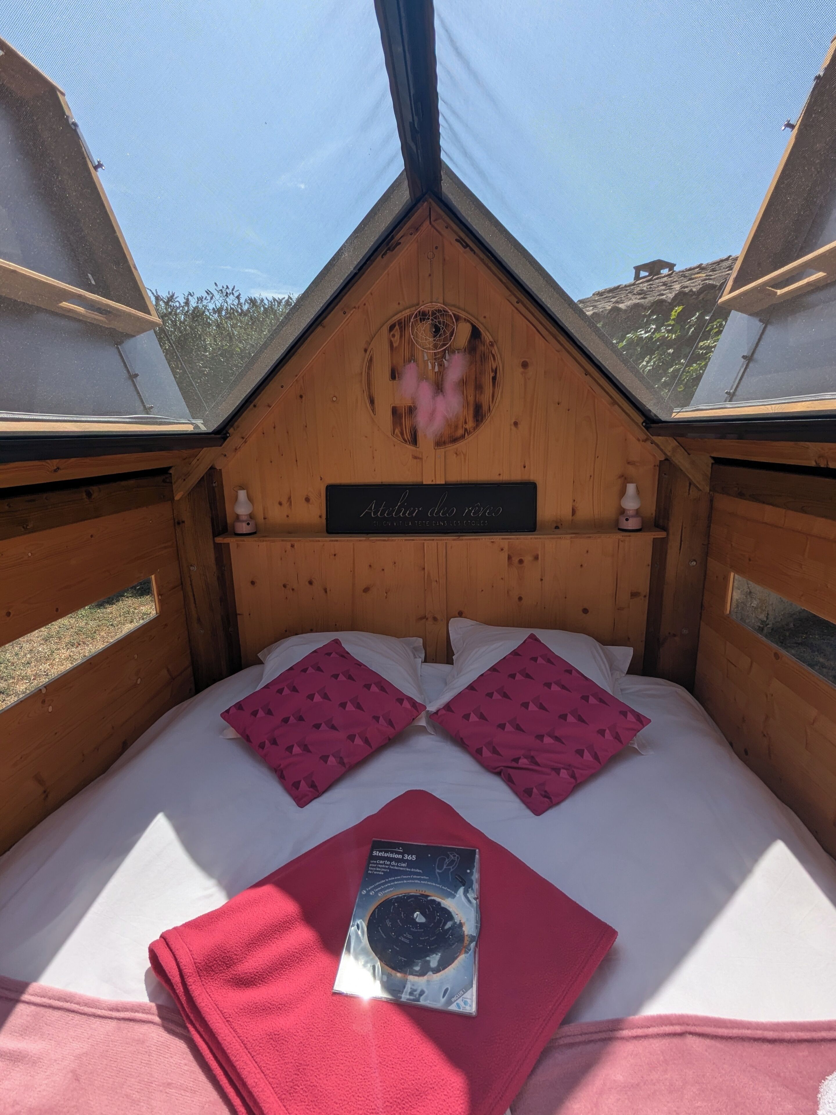 A cozy wooden bedroom with a skylight, two pink pillows, a red blanket, and a book on the bed.