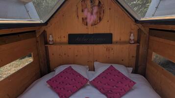 A cozy wooden bedroom with a skylight, two pink pillows, a red blanket, and a book on the bed.