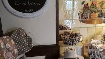 Una zona de cocina con un maniquí vestido con delantal de chef, una pizarra con notas escritas a mano y varios utensilios y alimentos exhibidos en estanterías.