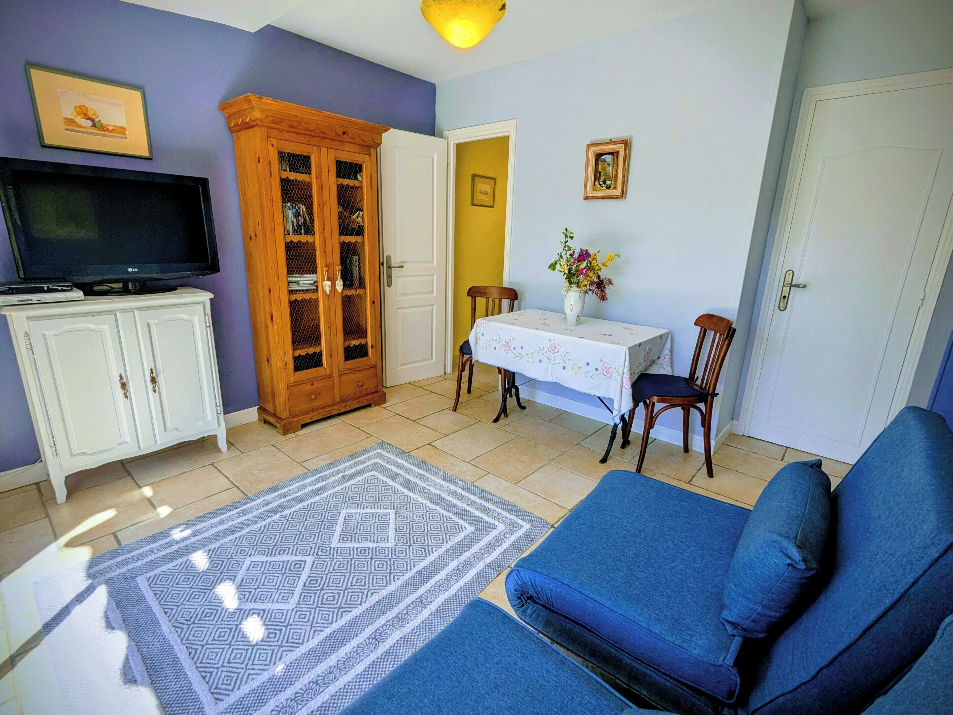 Una sala de estar con sofá, televisión sobre un mueble, una mesa de comedor con sillas y un aparador con puertas de cristal.