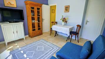 Un salon comprenant un canapé, un téléviseur posé sur un meuble, une table à manger avec des chaises et un buffet aux portes vitrées.