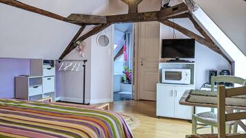 Un dormitorio acogedor en el ático con techo inclinado, una cama con manta a rayas coloridas, una silla de madera, una mesita pequeña y un televisor.