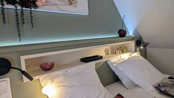 A neatly made bed with white linens and floral-patterned pillows, a bedside table with a lamp, and a wall-mounted decorative item.