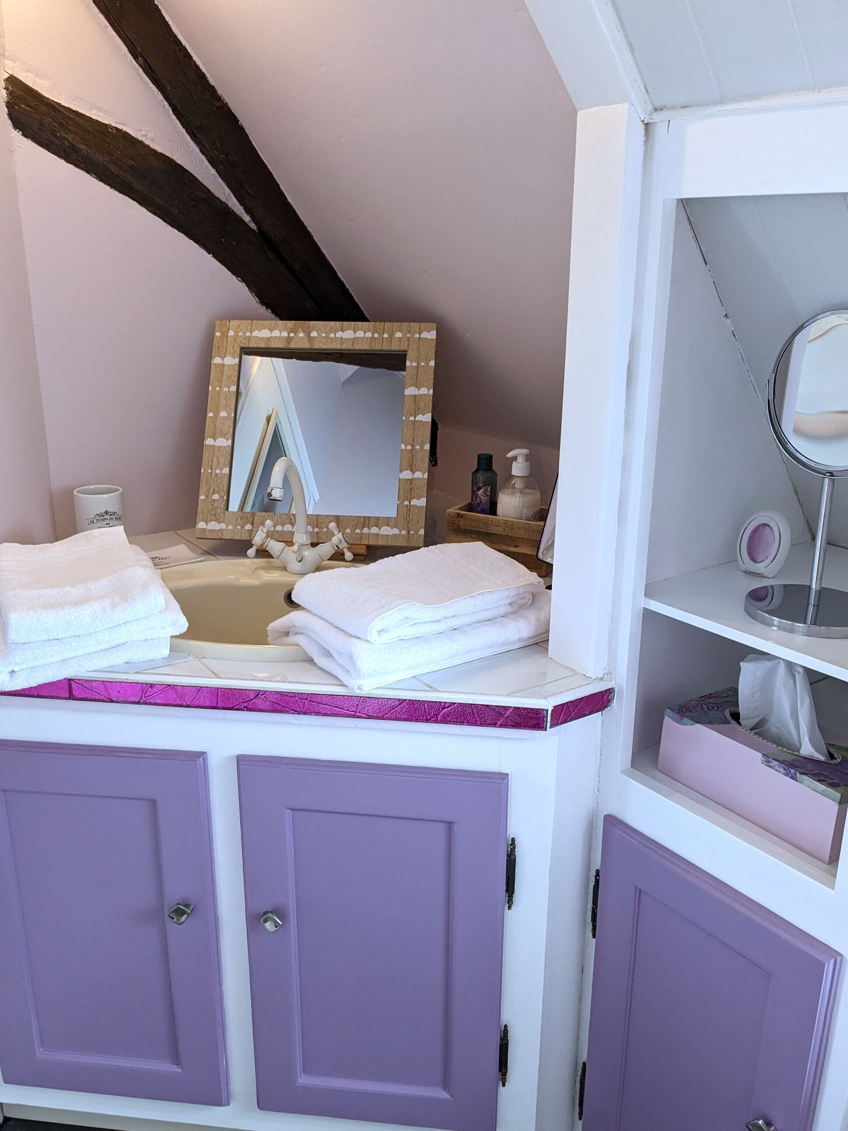 A bathroom with a vanity, a mirror, and a sink. There are towels stacked on the vanity, and a bottle of hand soap on the sink.