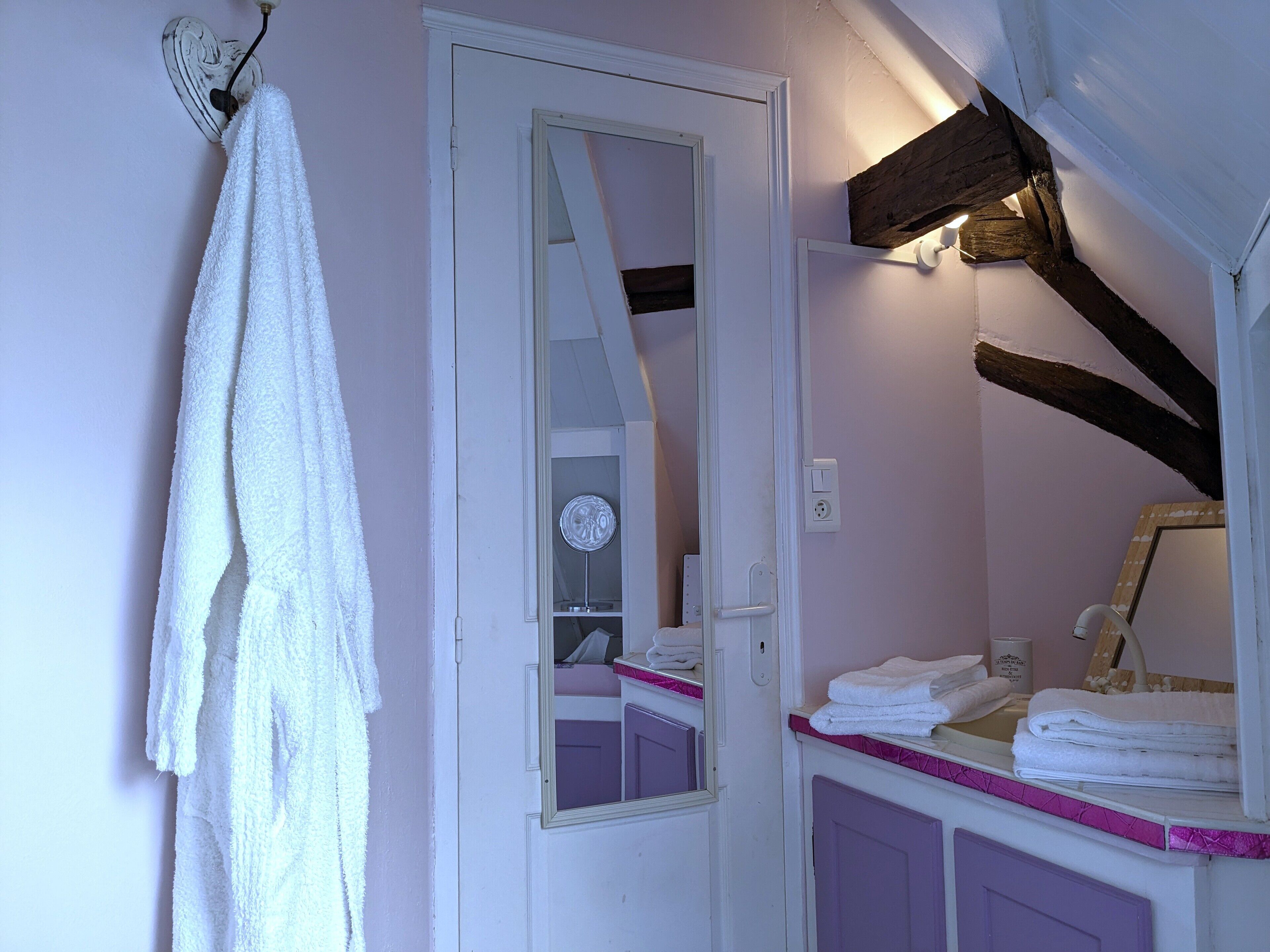 A bathroom with a white towel hanging on a wall-mounted rack, a mirror, and a sink area with stacked towels.