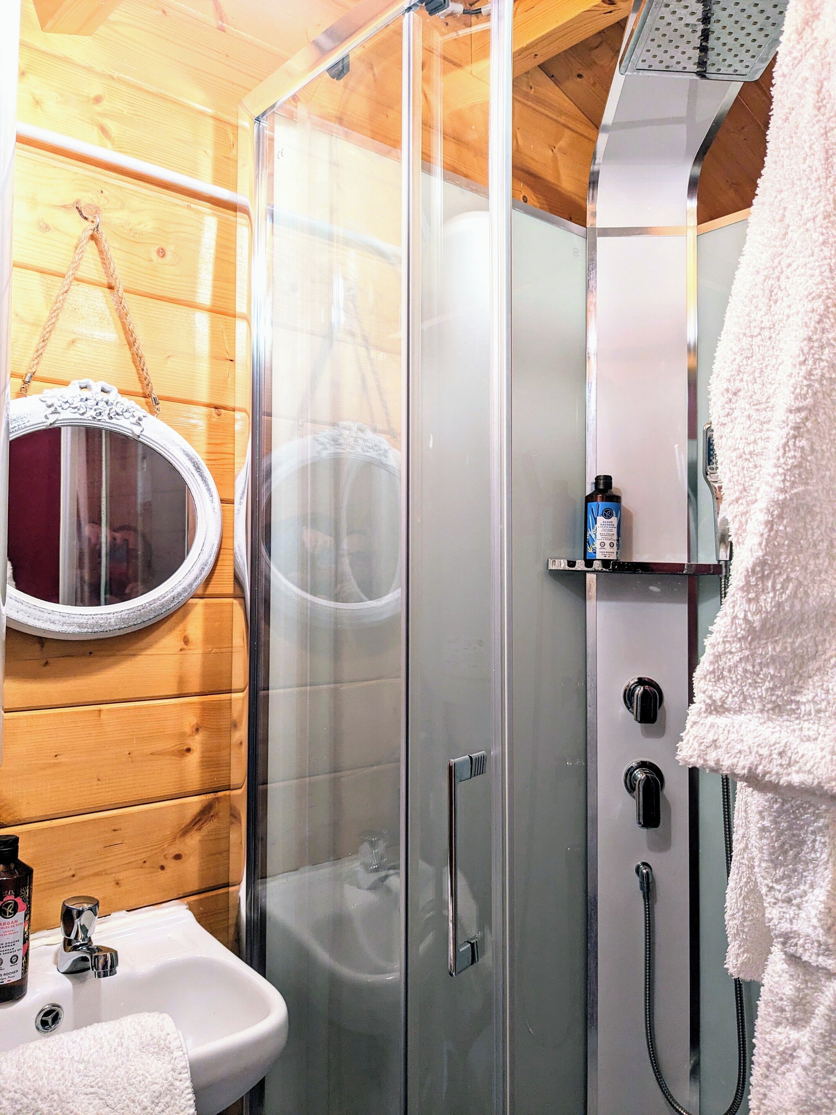 A bathroom with a glass shower enclosure, a white sink, and a mirror with a decorative frame.