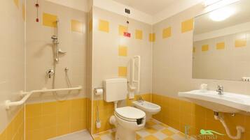 Un baño con azulejos amarillos y blancos, ducha, inodoro, bidé y lavamanos.