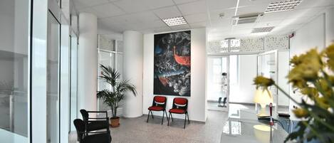 A modern office space with glass walls, a large abstract painting, and a reception desk with a lamp.