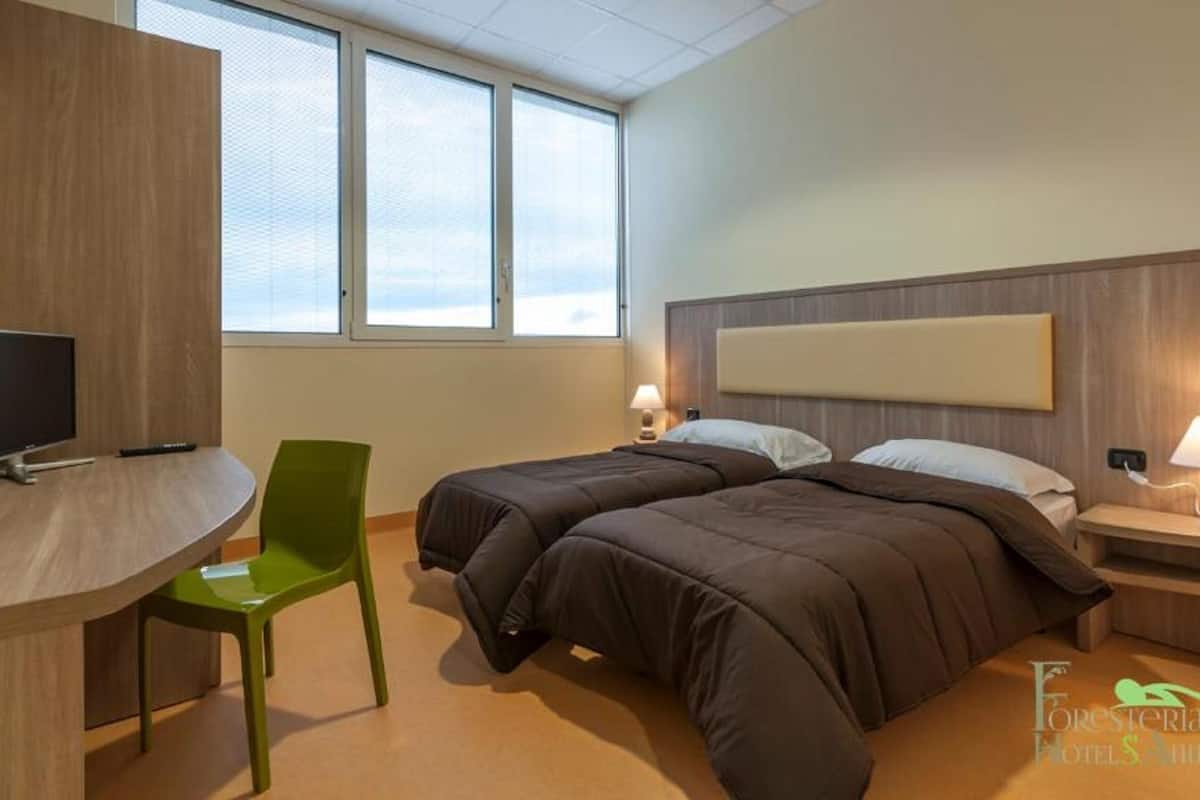 Habitación de hotel con dos camas, un escritorio, una silla y un televisor.