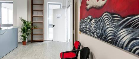 A reception area with a modern design, featuring a reception desk, a seating area with chairs, a bookshelf, and a large abstract painting on the wall.