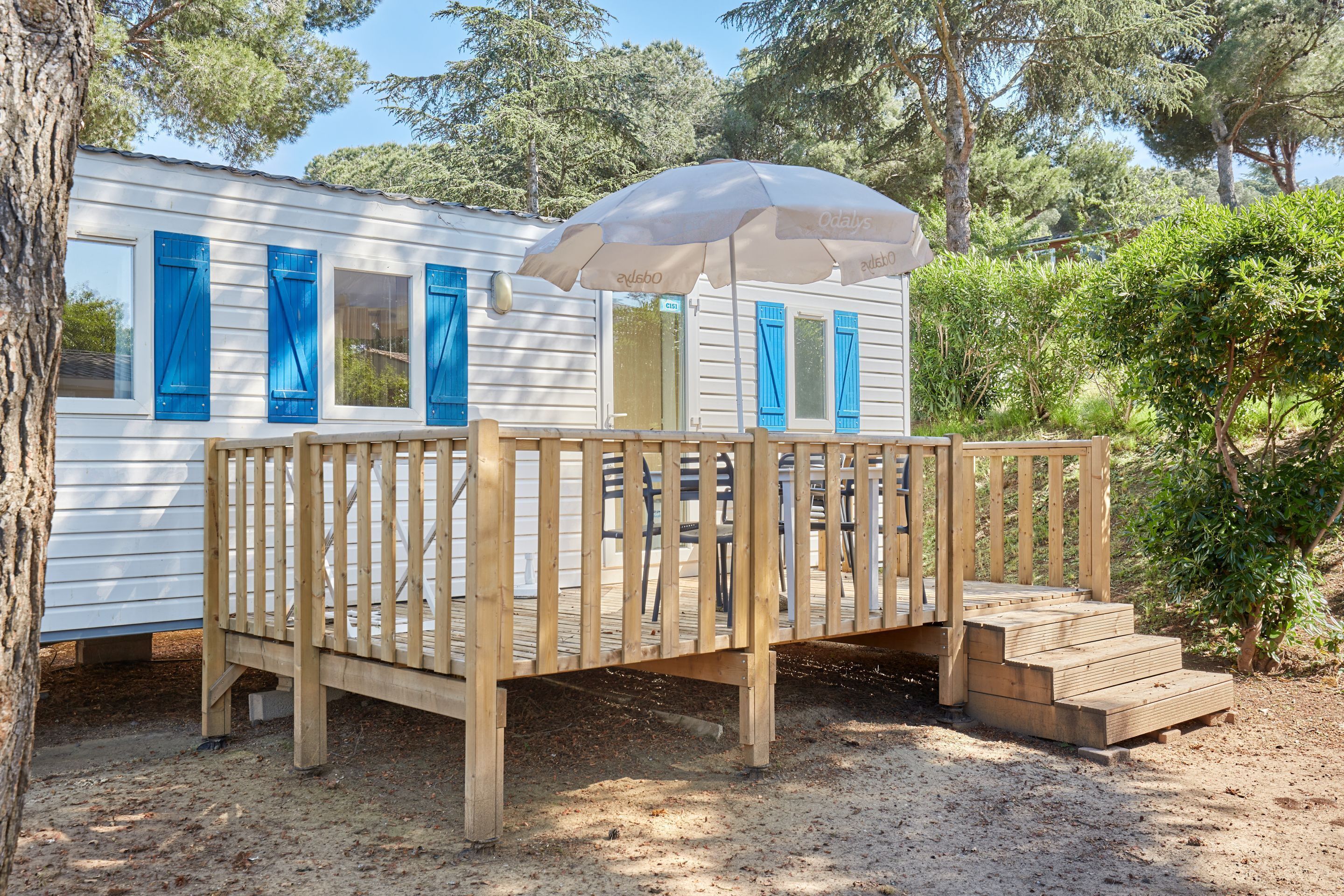 A wooden deck with a white building in the background, a wooden fence, and a large umbrella.