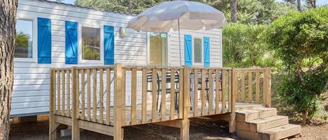 A wooden deck with a white building in the background, a wooden fence, and a large umbrella.