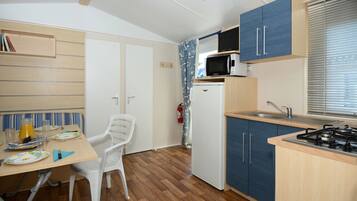 A compact kitchen with a microwave, stove, and sink. There is a dining table with chairs and a small refrigerator.