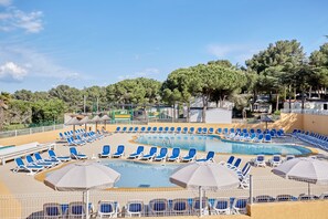 A pool area with multiple lounge chairs and umbrellas, surrounded by a fence. - Domaine Résidentiel de Plein Air Odalys La Pinède (Agde)