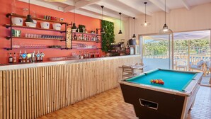 A bar area with a pool table, wooden slat wall, and shelves with bottles and glasses. - Domaine Résidentiel de Plein Air Odalys La Pinède (Agde)