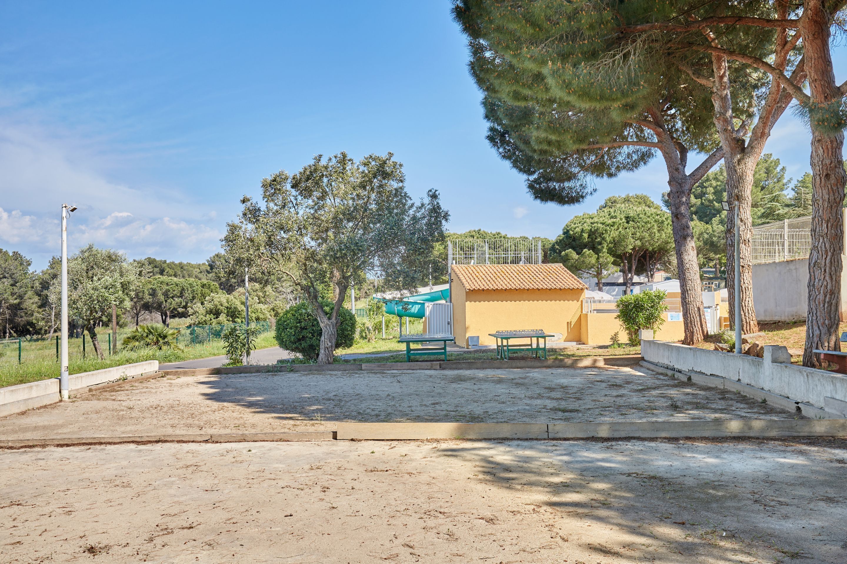 A sandy outdoor area with a building, trees, and a fence.