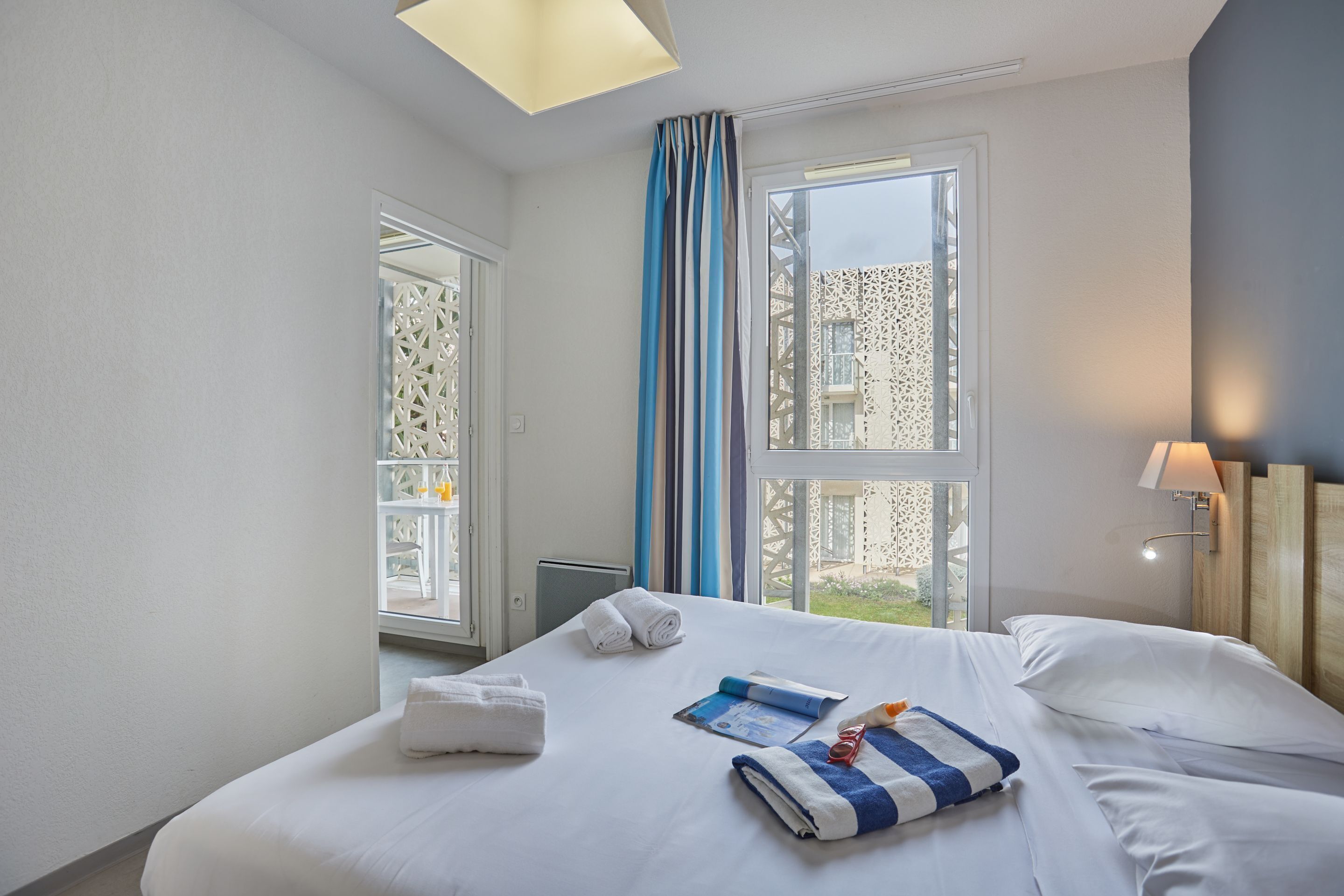 Ein Hotelzimmer mit einem großen Bett, einem Fenster mit Vorhängen, einem Nachttisch und einer Lampe.