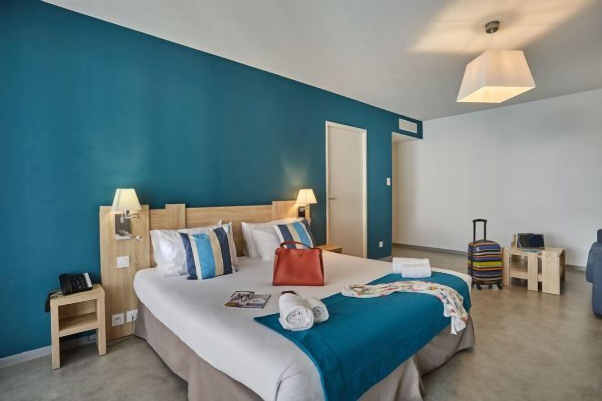 Une chambre d’hôtel avec un grand lit, deux tables de chevet, une valise, un téléviseur et une lampe.