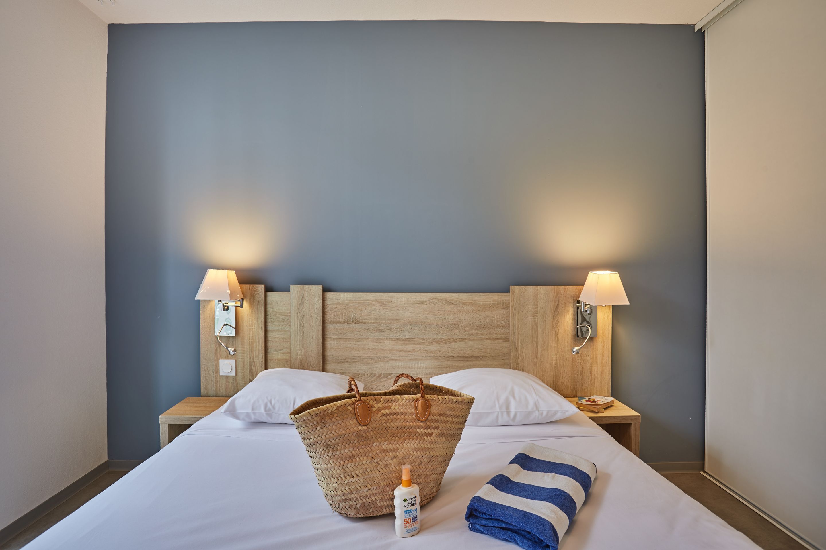 Een hotelkamer met een groot bed, twee bedlampen, een houten hoofdeinde en een geweven mand op het bed.