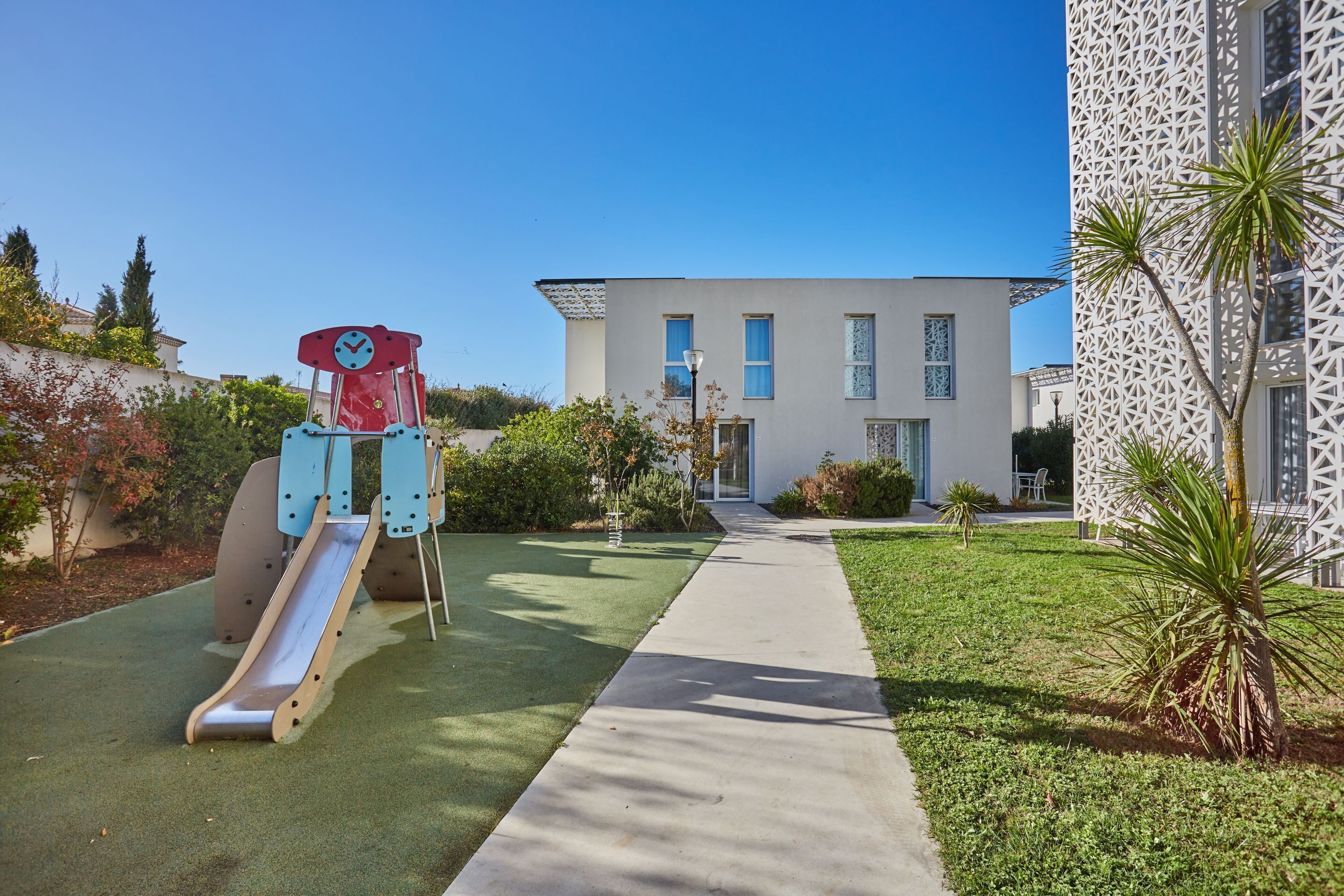A playground with a slide and a building with a geometric facade in the background.