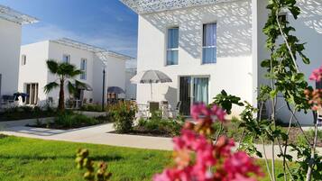 A modern white building with a patio area, outdoor seating, and a well-maintained garden.