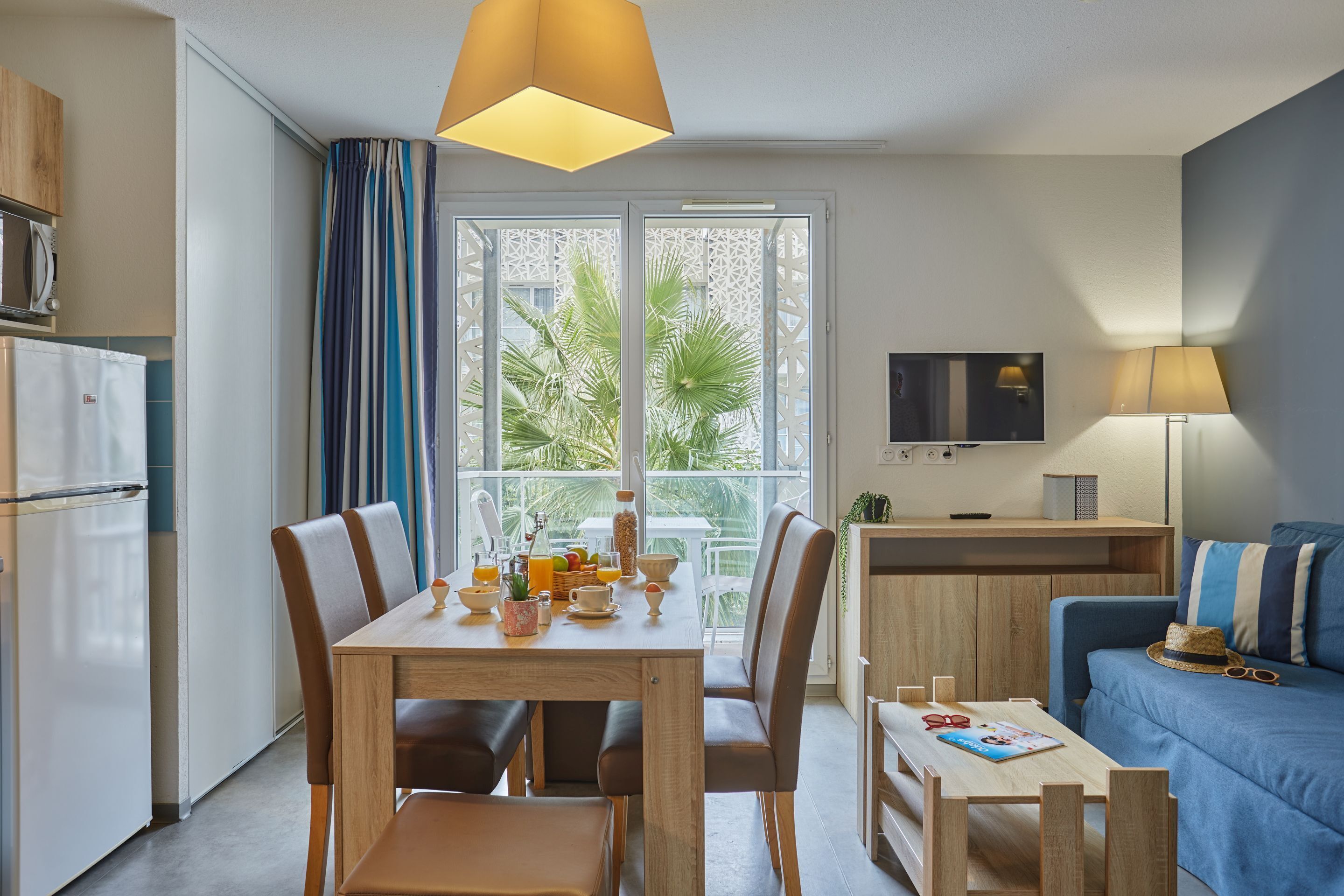 Un espace de vie compact comprenant une table à manger, des chaises, un canapé, un téléviseur et un coin cuisine équipé d’un four à micro-ondes et d’un réfrigérateur.